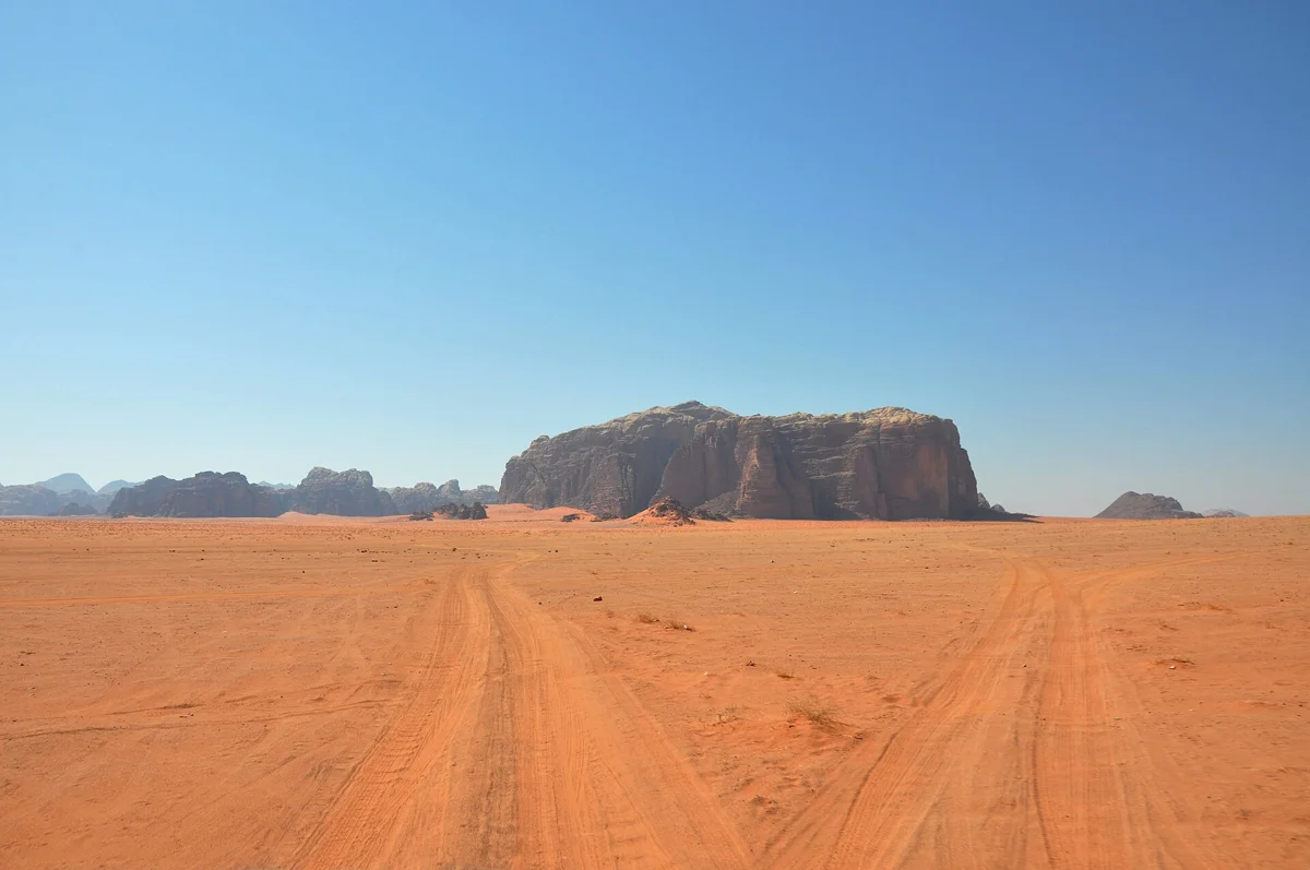 Jeep tracks across the sand toward a lone rock on a Wadi Rum half day jeep tour